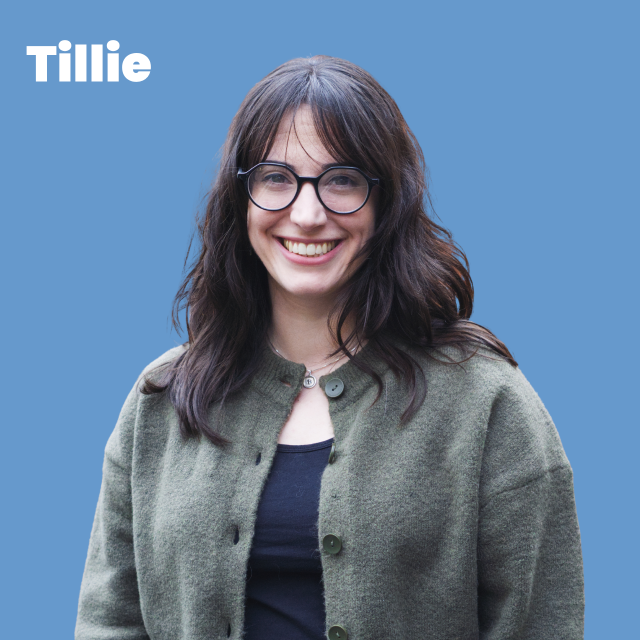 Picture of Tille, white woman, shoulder length black hair, glasses, wearing a green cardigan with a black t shirt underneath